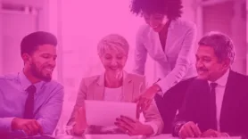 Four coworkers gathered around a table, examining information on a tablet device.