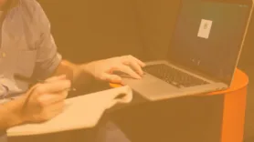 Man with a notebook and pen, sitting in front of laptop.