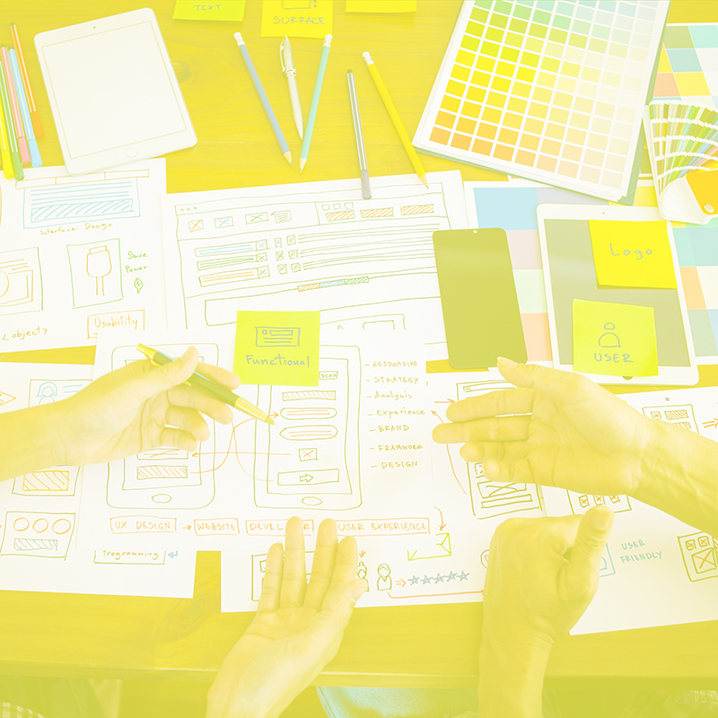 Hands working over a desk covered in papers, devices